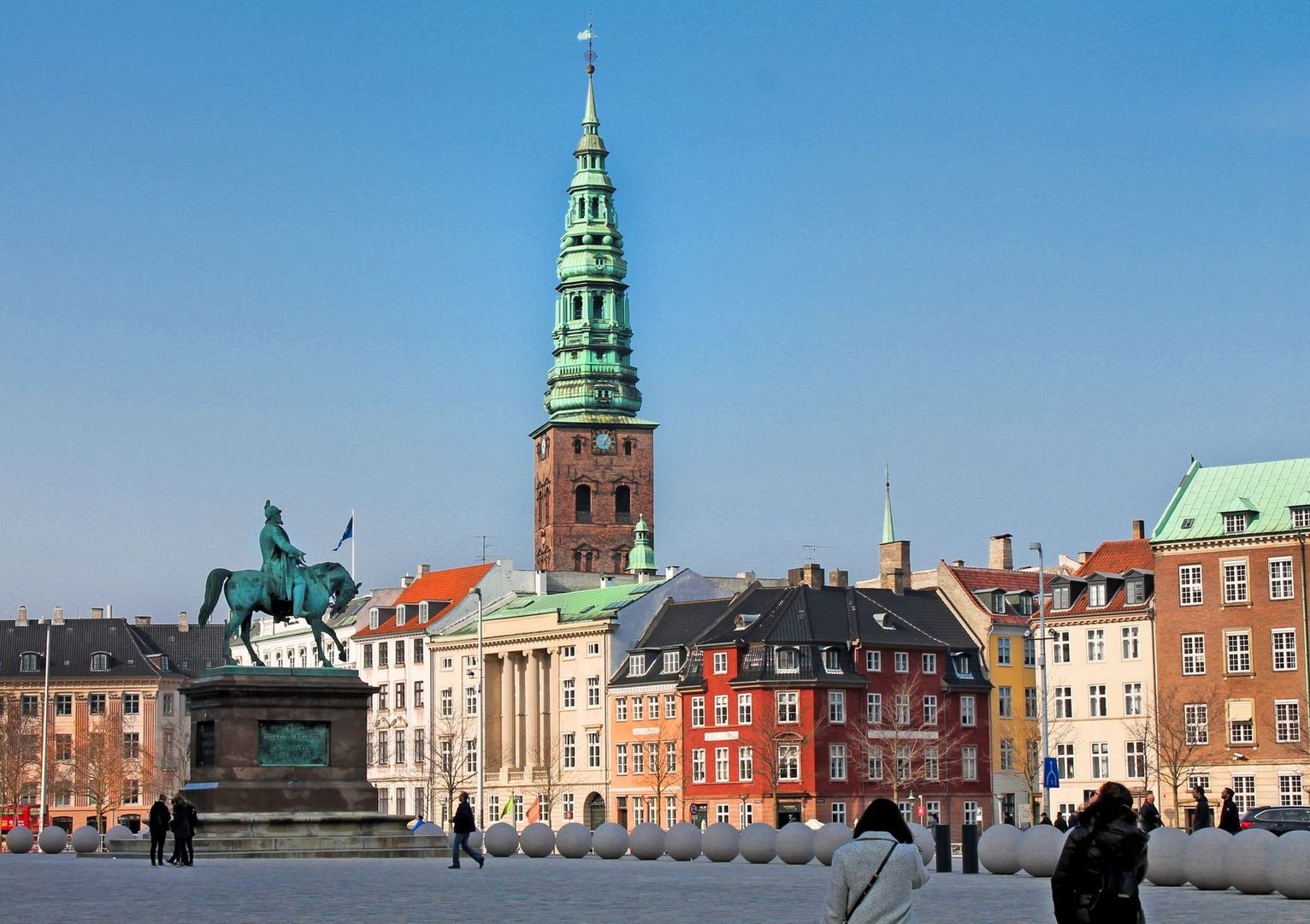 Stadsvy med ryttarstaty och en hög kyrkspira mot blå himmel