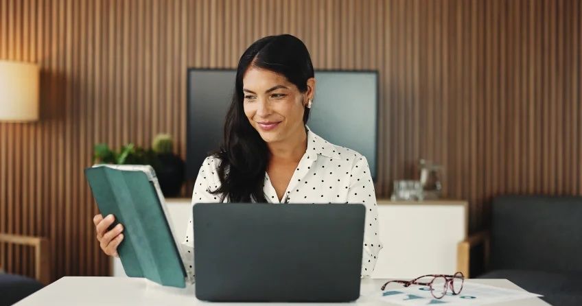 Affärskvinna arbetar vid laptop och håller en surfplatta på kontoret